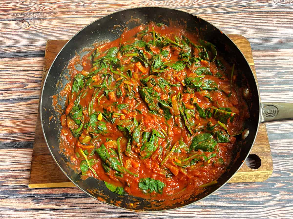 Curry sauce in a pan with spinach stirred in.