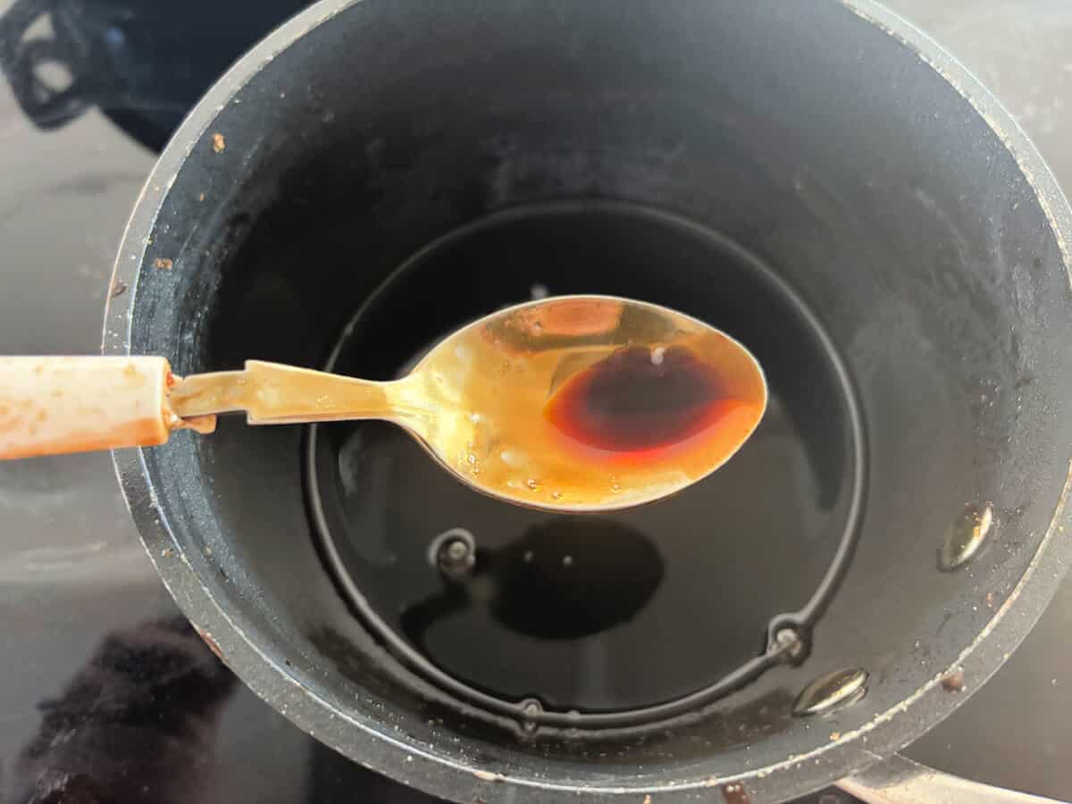 Teriyaki sauce in a spoon above a small saucepan.