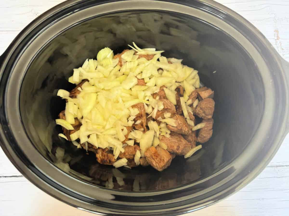 Beef and diced onion in slow cooker pot.