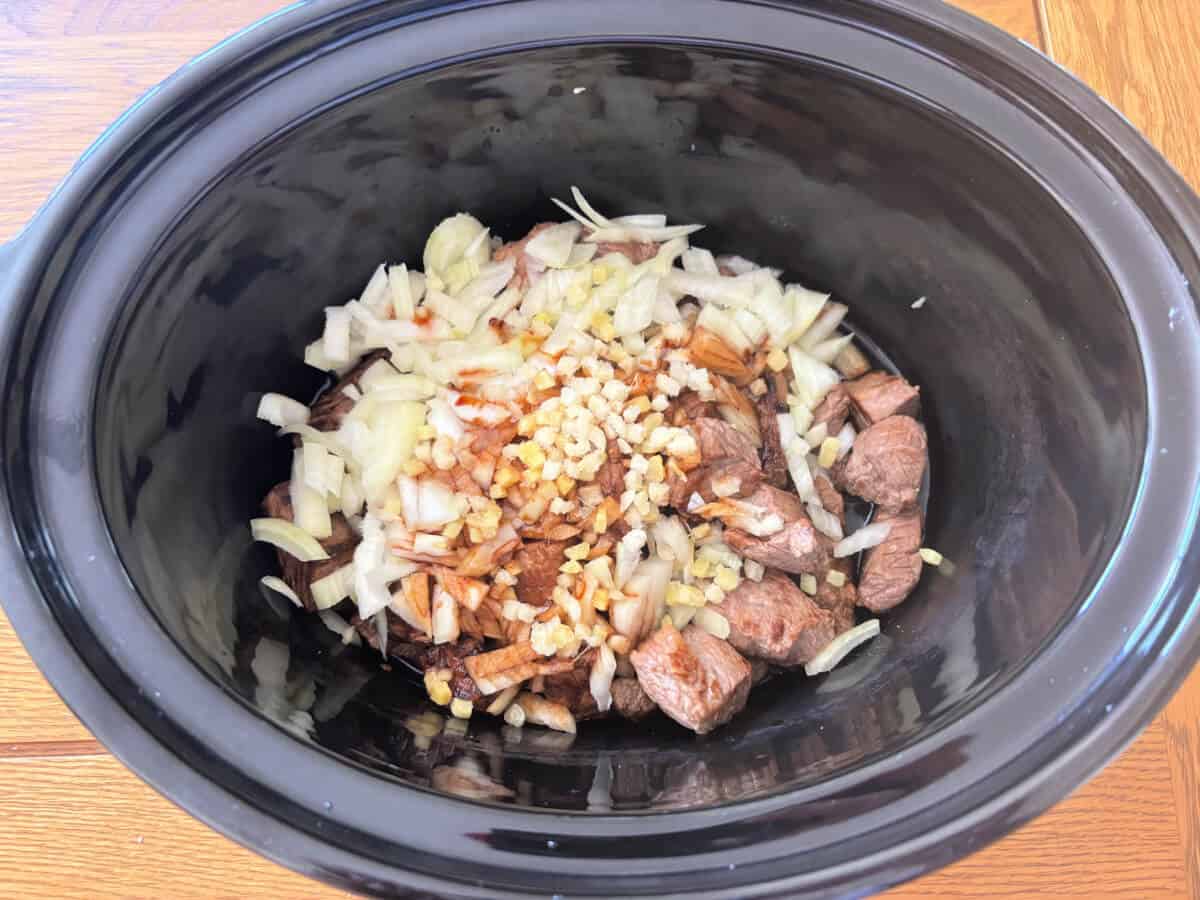 Beef, diced onion, garlic and ginger in slow cooker pot with homemade teriyaki sauce.