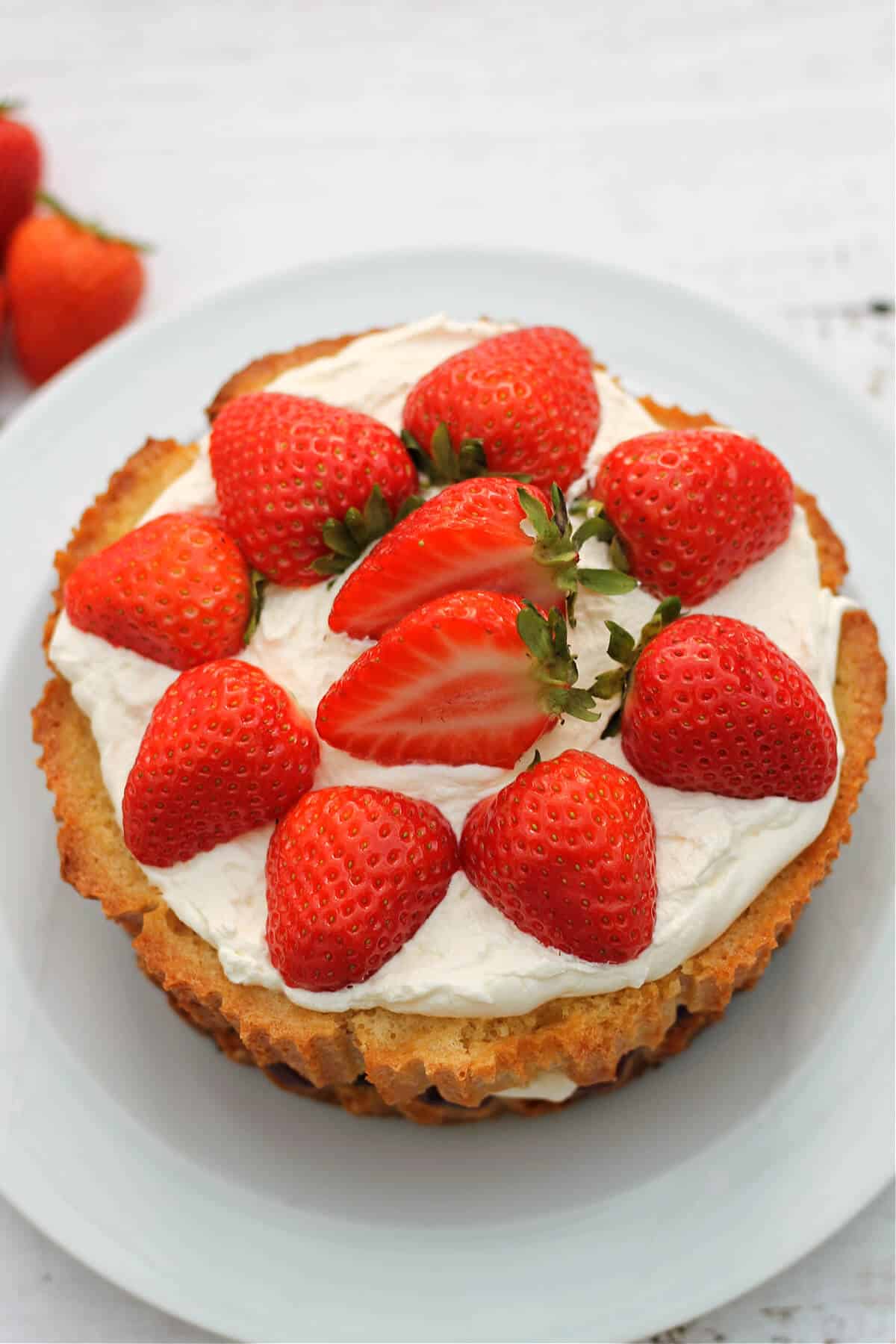 A sponge cake topped with cream and strawberries on a white plate.
