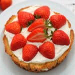 √ A Victoria sponge cake topped with cream and strawberries on a white plate.