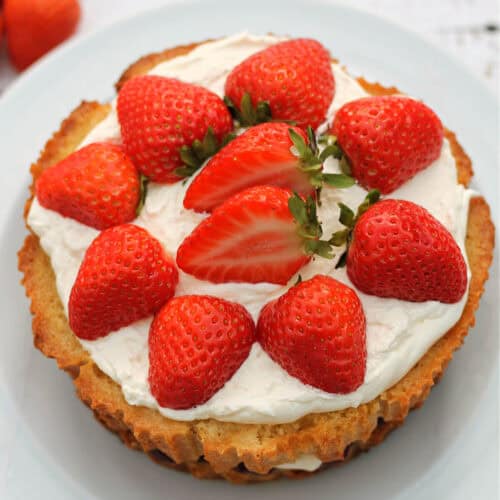 √ A Victoria sponge cake topped with cream and strawberries on a white plate.