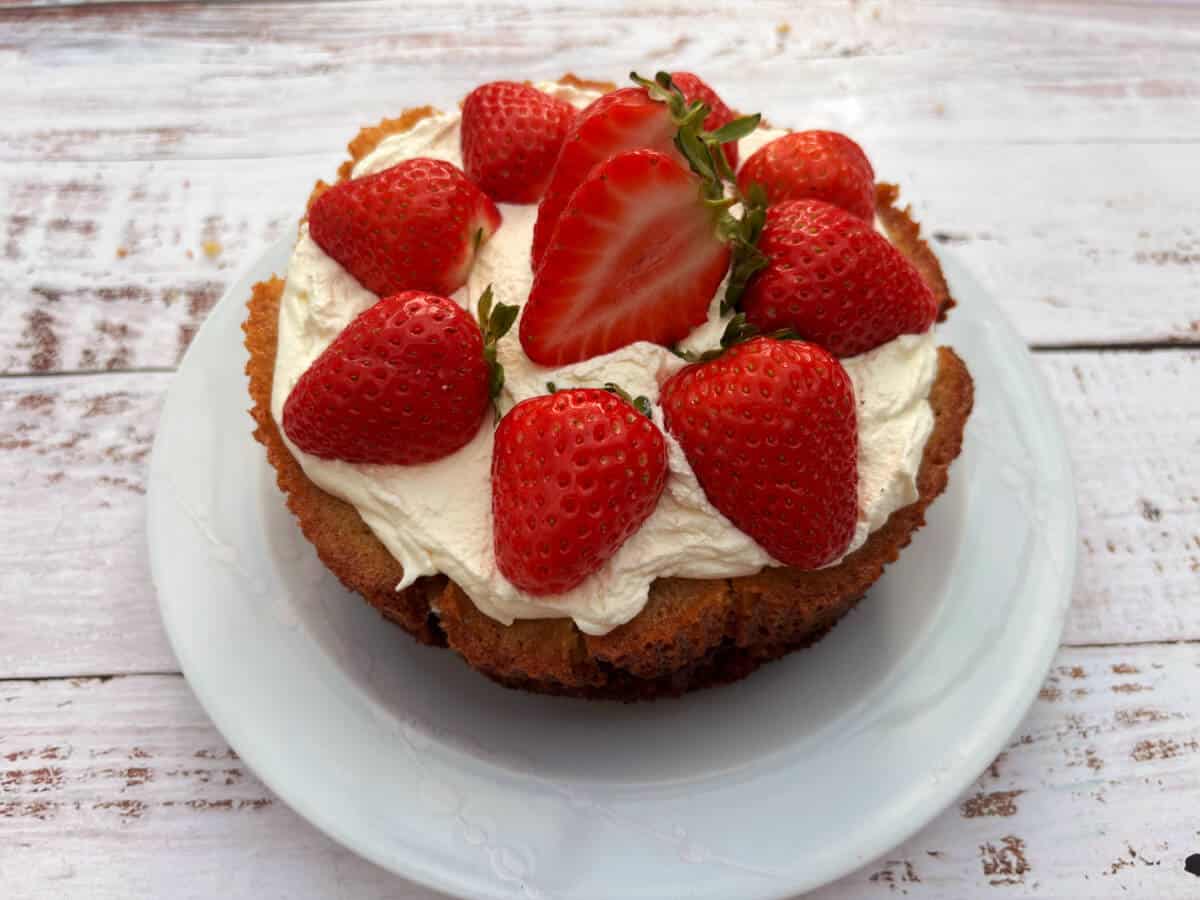 Cake with layer of whipped cream and halved strawberries added on top, on a white plate.