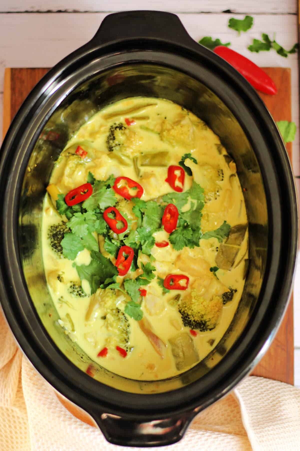 Slow cooker fish curry with fresh herbs and chilli as garnish, in pot.