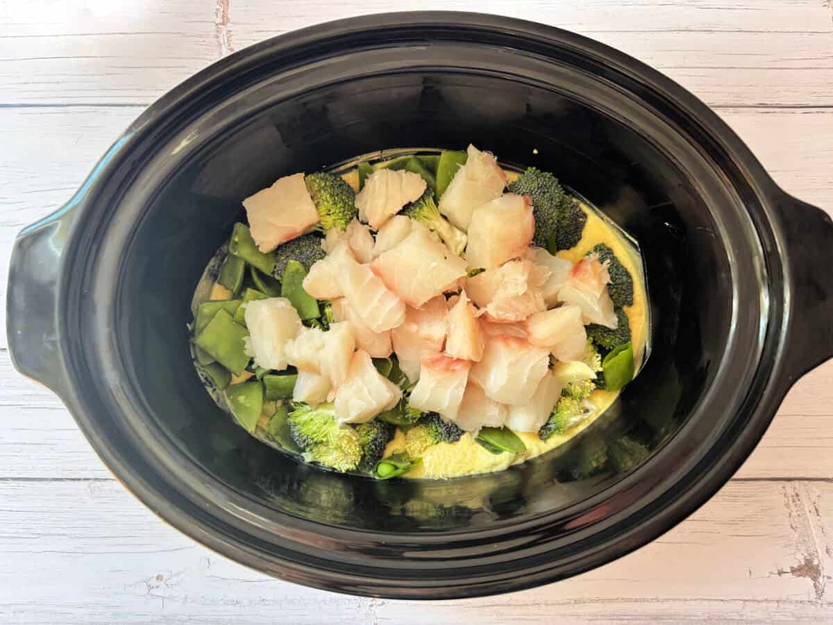 Cubed fish with veggies in slow cooker pot with coconut milk sauce.