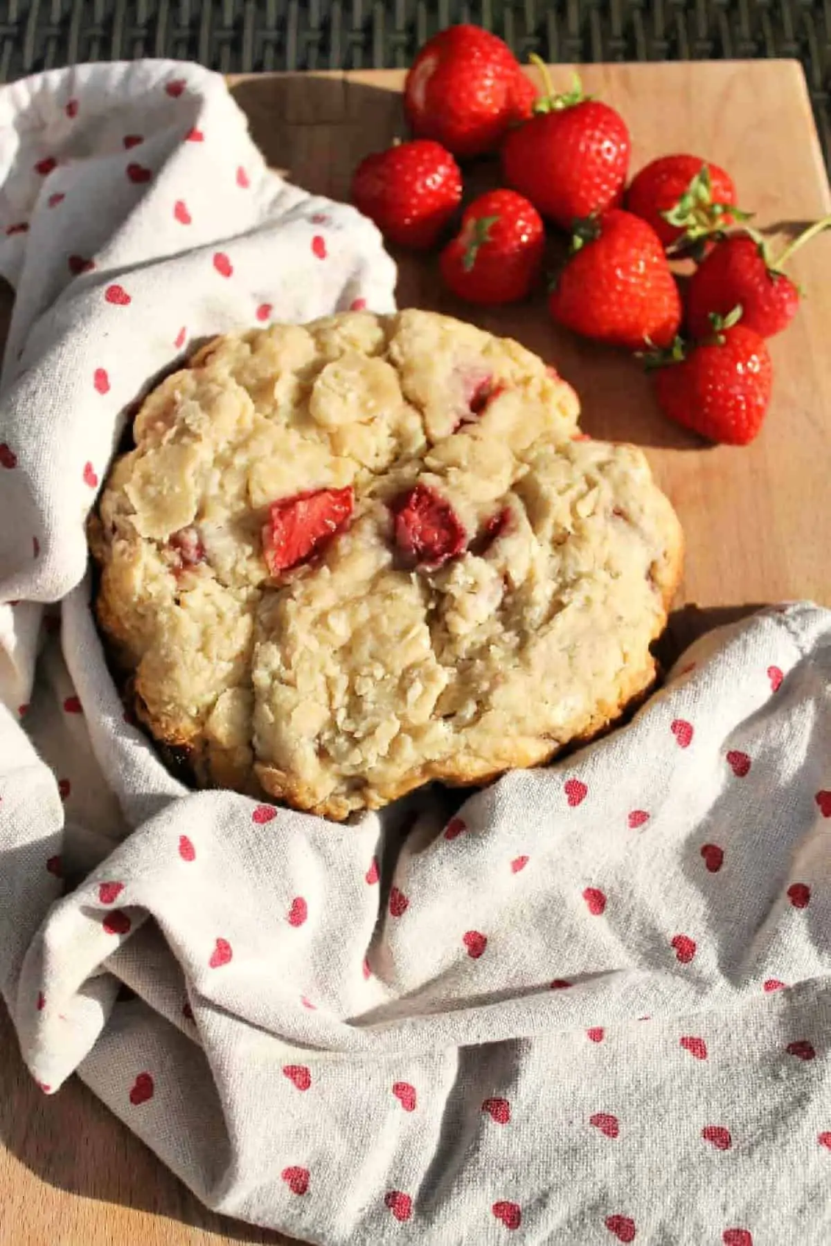 Large scone with strawberries on a board on a tea towel, with strawberries to the side.