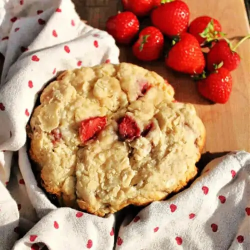 Close up of a large strawberry scone cake on wooden board, strawberries on the side.
