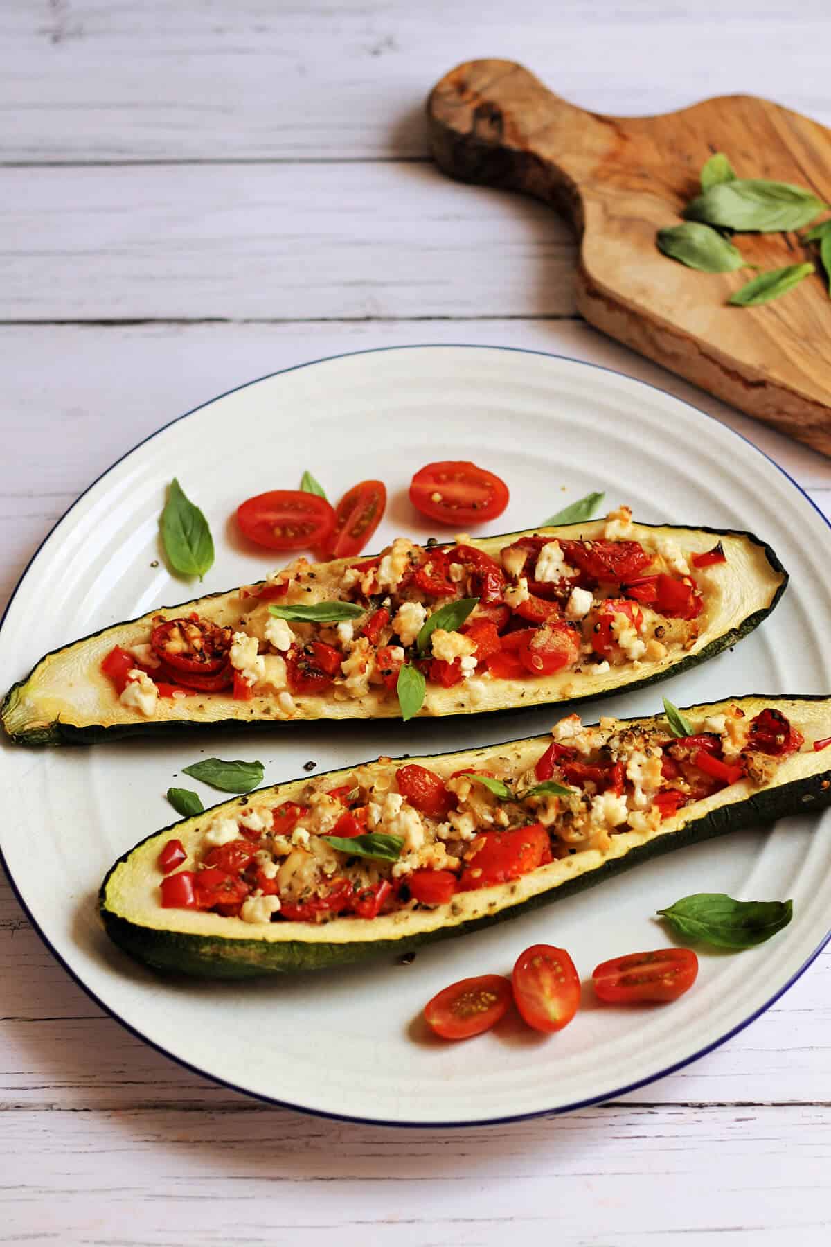 Two stuffed courgettes on a white plate, fulled with tomato, pepper and feta on top.