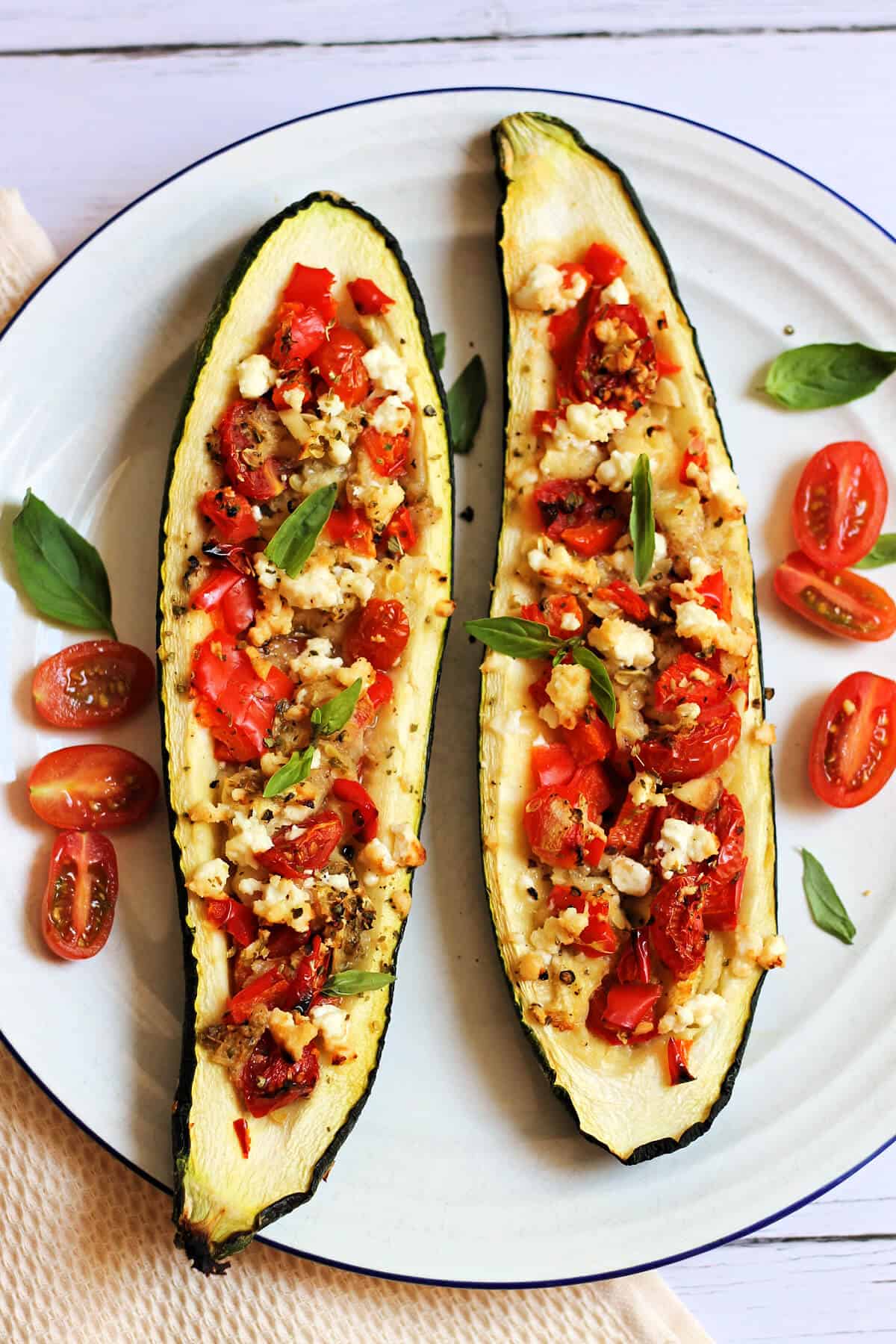 Two stuffed courgettes on a plate garnished with fresh basil leaves.