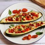 Two stuffed courgettes on a white plate, fulled with tomato, pepper and feta on top.