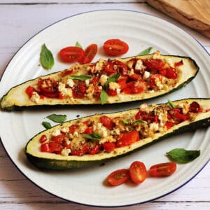 Two stuffed courgettes on a white plate, fulled with tomato, pepper and feta on top.