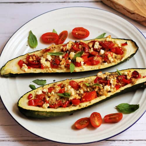 Two stuffed courgettes on a white plate, fulled with tomato, pepper and feta on top.