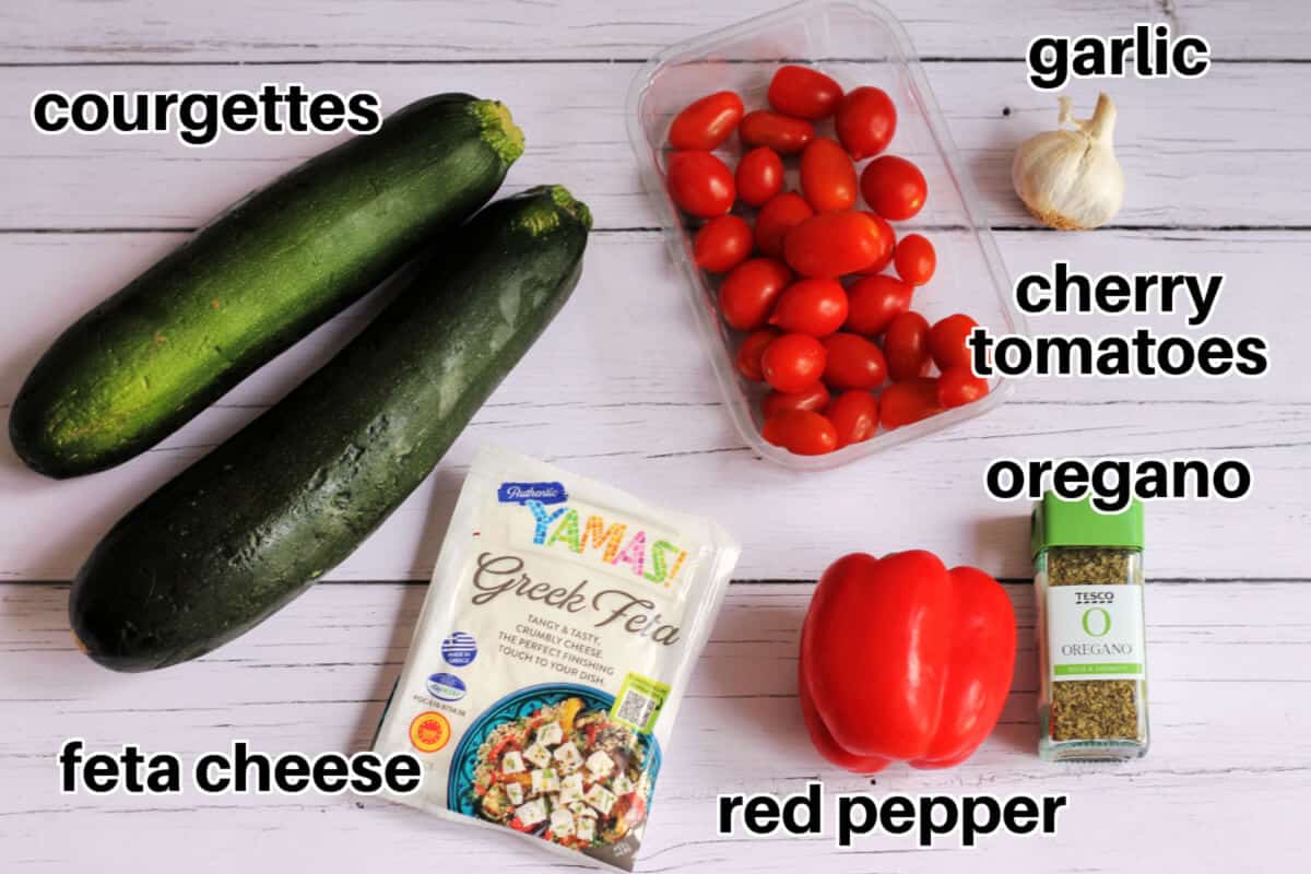 Ingredients for stuffed courgettes, on white surface, with text labels.