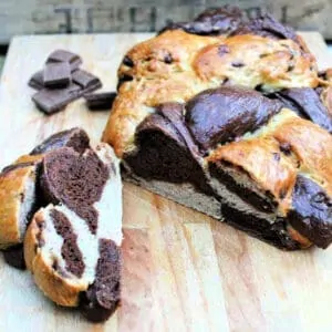 Two-tone dark brown and white challah bread sliced open on a cutting board.