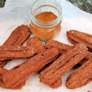 Churros on white baking paper, with a jar of pumpkin spice.