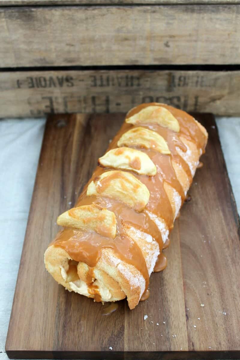Cake roll with apple and caramel on a wooden board.