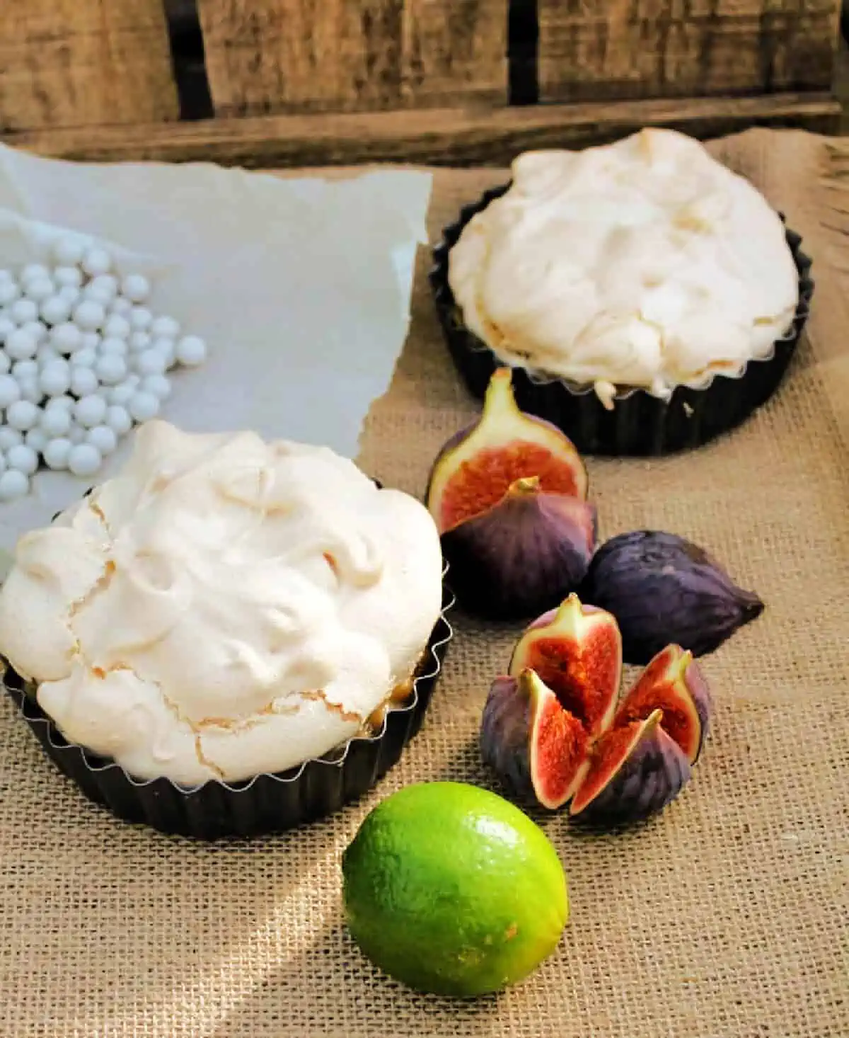 Two meringue pies on a hessian cloth with a lime and fresh figs to the side.