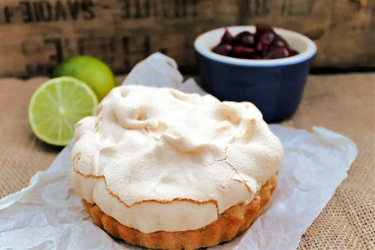 Meringue pie with limes and cherries in the background,