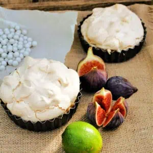 Meringue pies on a hessian cloth, lime and figs to the side.