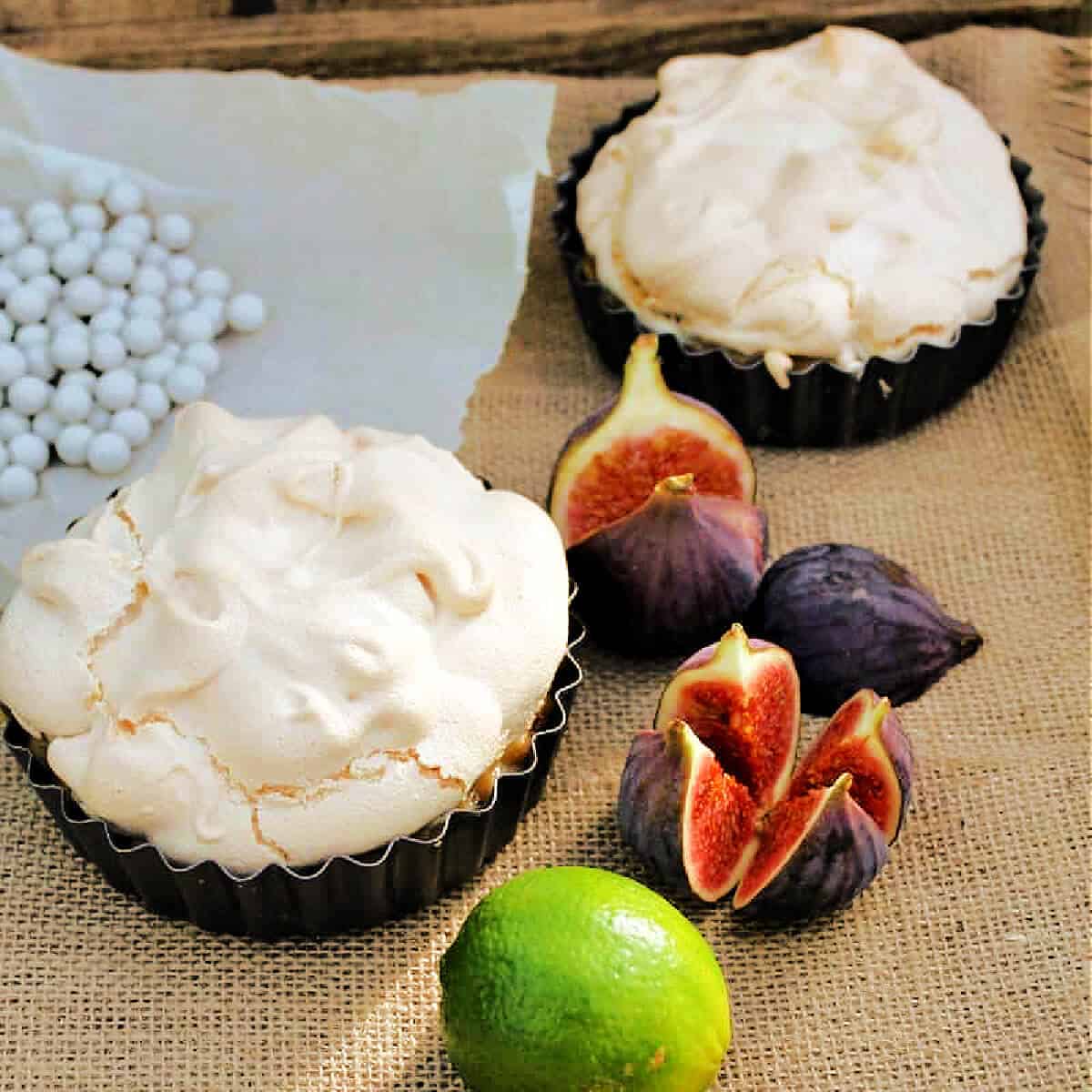 Meringue pies on a hessian cloth, lime and figs to the side.