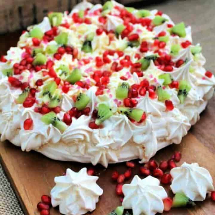 Festive pavlova topped with red and green fruit, with piped decoration.
