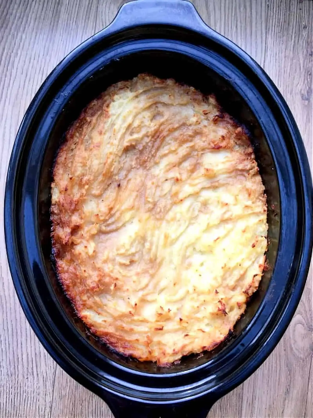 View of cottage pie with browned top in slow cooker pot.