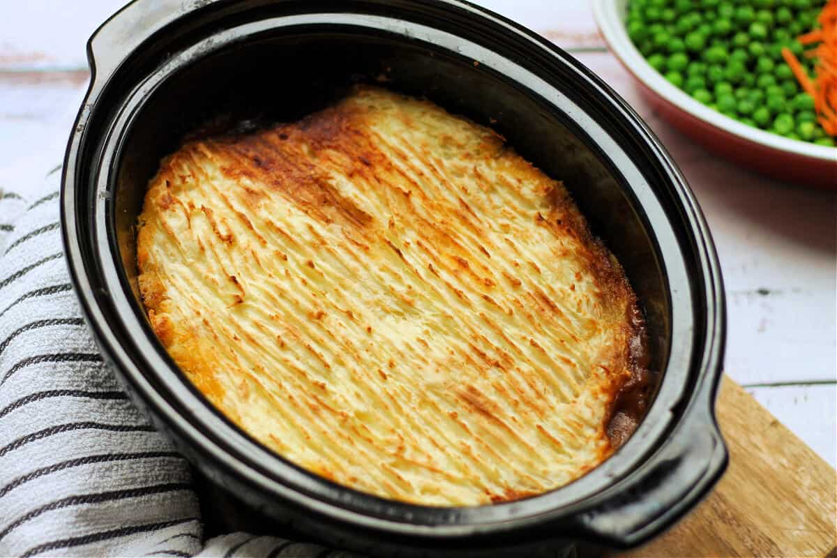Slow cooker pot of cottage pie with browned mash topping.