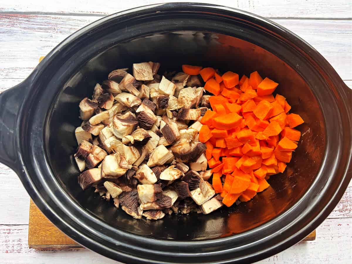 Chopped mushrooms and carrots in slow cooker pot.