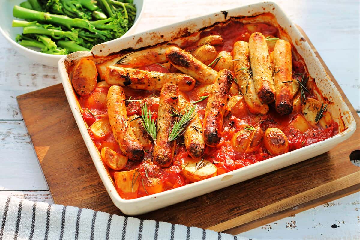 Sausage and potato bake in a white serving dish, bowl of broccoli behind.