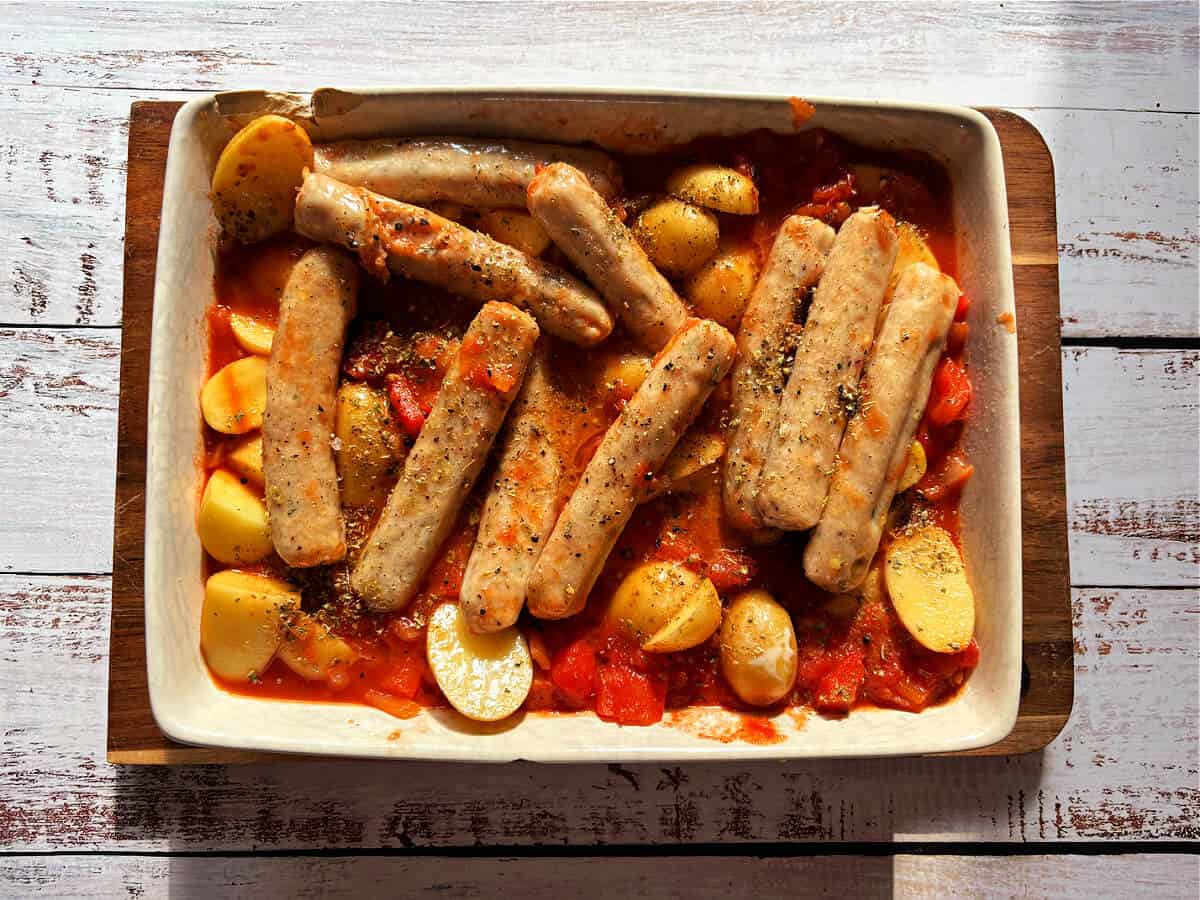 Sausage and potato bake in a white dish, before cooking.