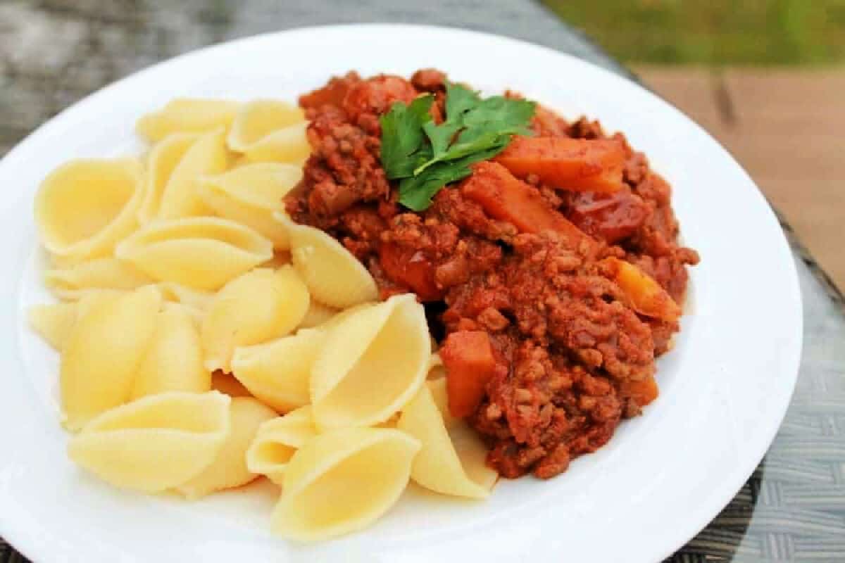 Bolognese with pasta shells on a white plate.
