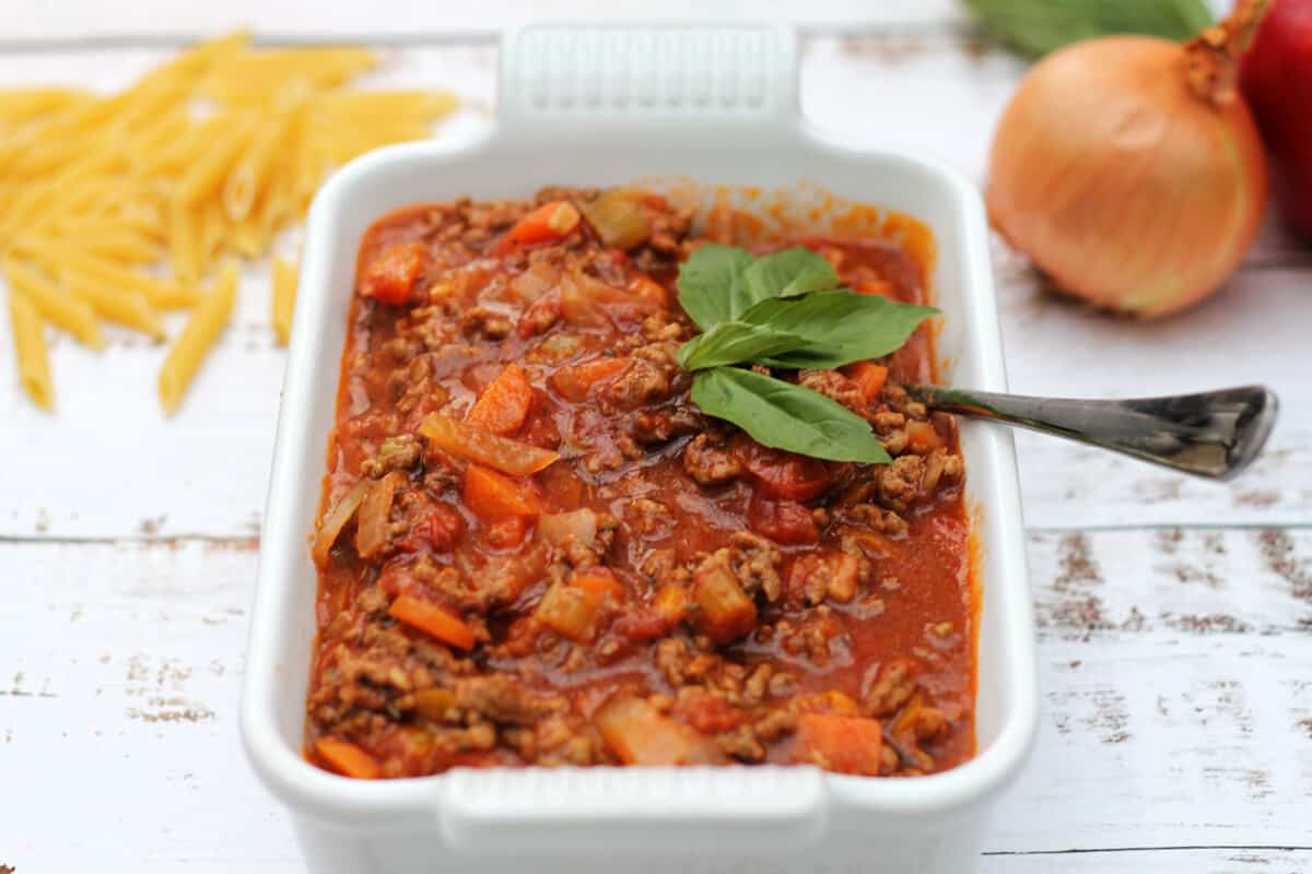 Bolognese sauce in a white serving dish, garnished with basil.
