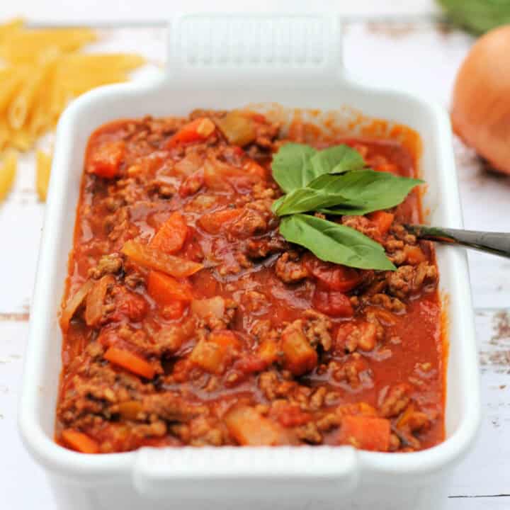 Bolognese sauce in a white serving dish, garnished with basil.