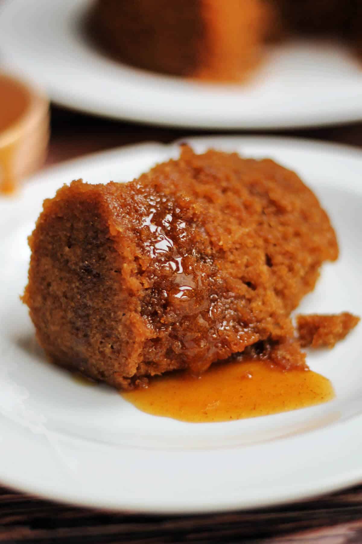 A white plate with a portion of gingerbread pudding with syrup.