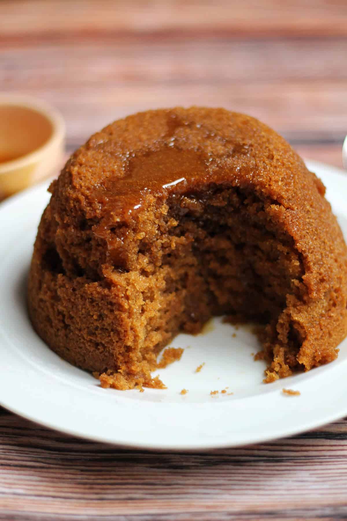 Soft brown gingerbread spice pudding on a white plate, with syrup drizzled over the top.
