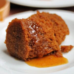 A white plate with a portion of gingerbread pudding with syrup.