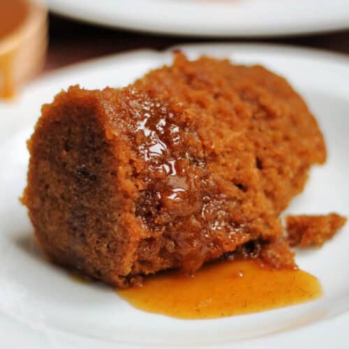 A white plate with a portion of gingerbread pudding with syrup.