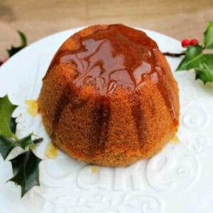 Steamed pudding covered in golden syrup on white plate with holly decoration.