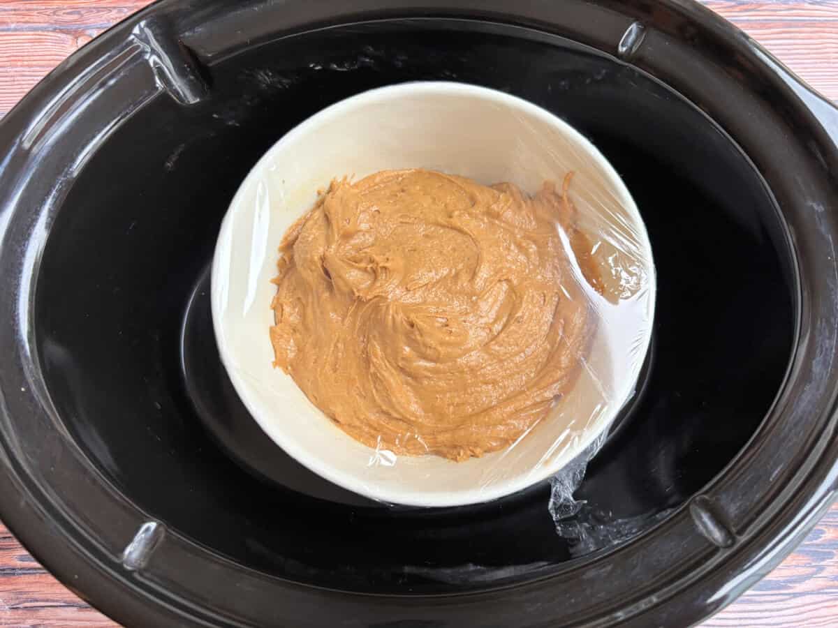 Pudding bowl covered with clingfilm in slow cooker pot.