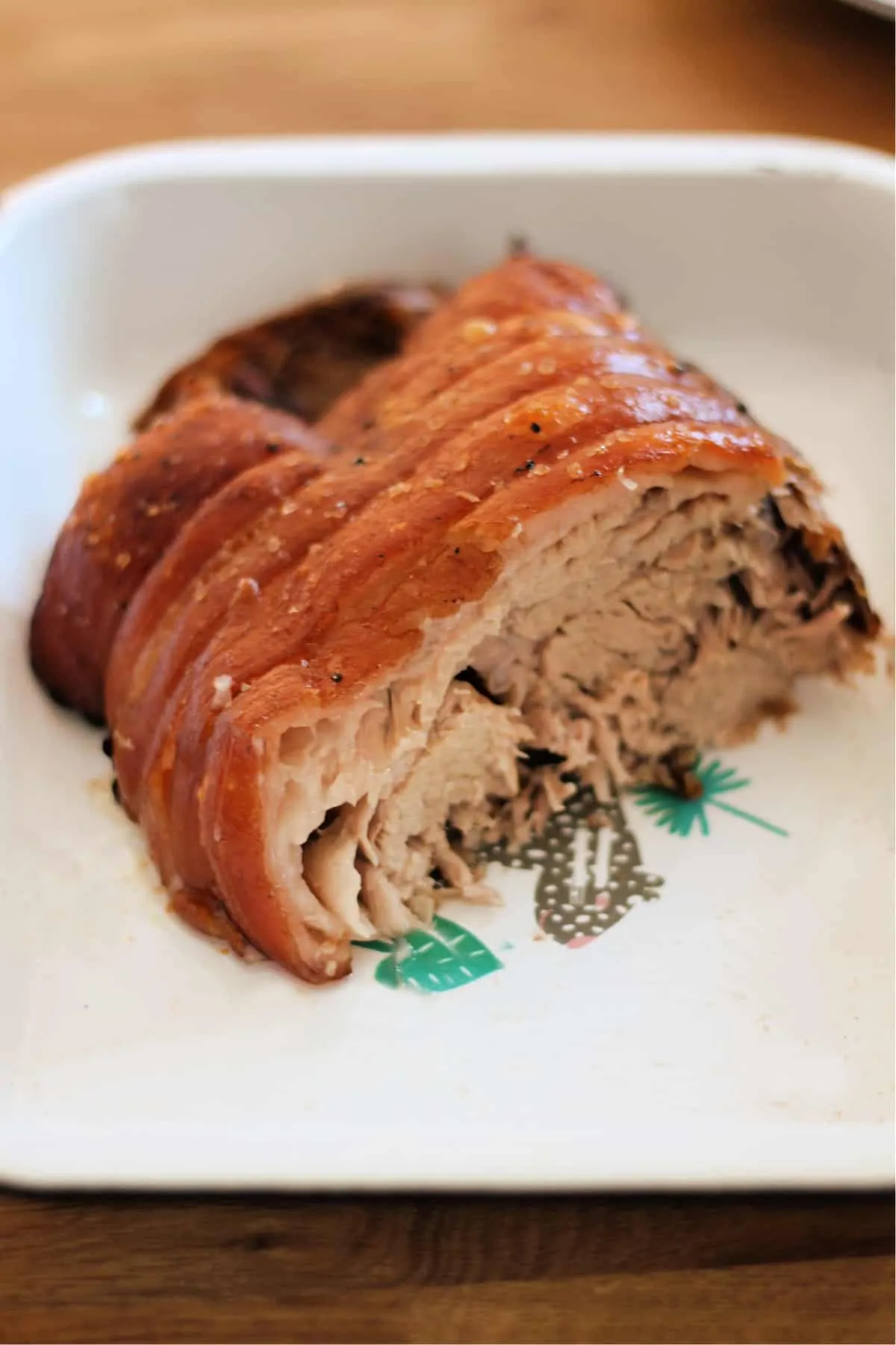 Roast pork joint in a serving dish, showing the soft meat inside.