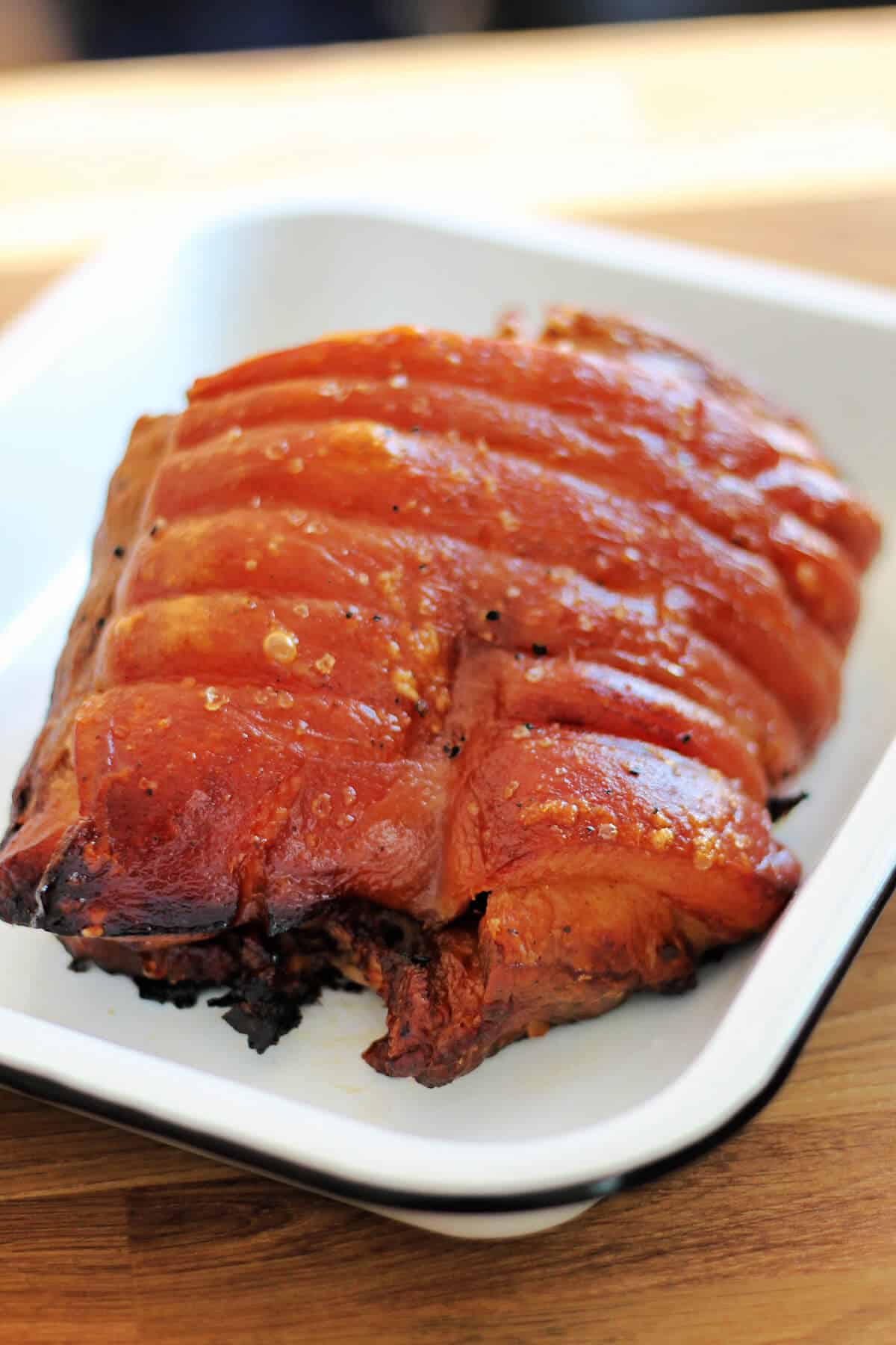 Roast pork joint with crispy crackling in a white enamel serving dish.