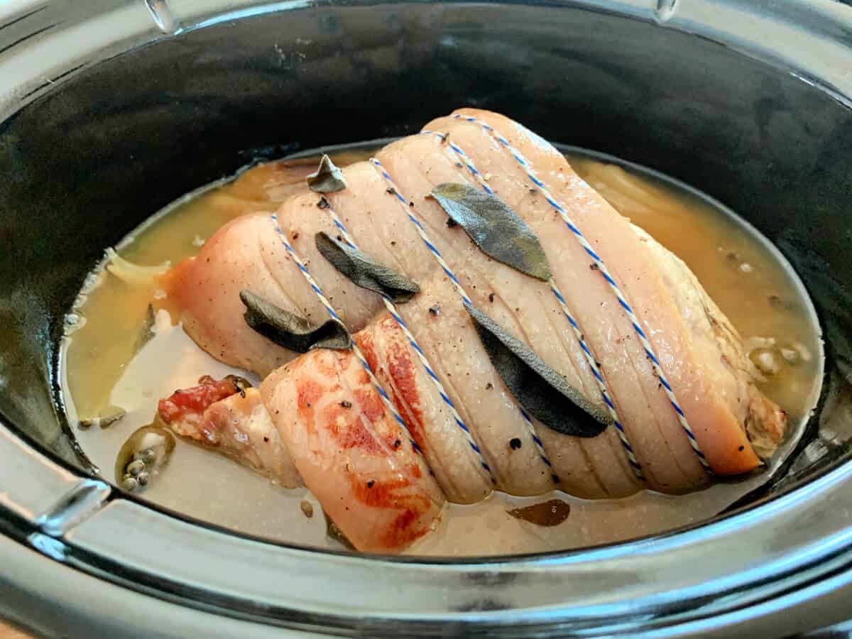 Cooked pork joint in slow cooker pot, in meat juices.