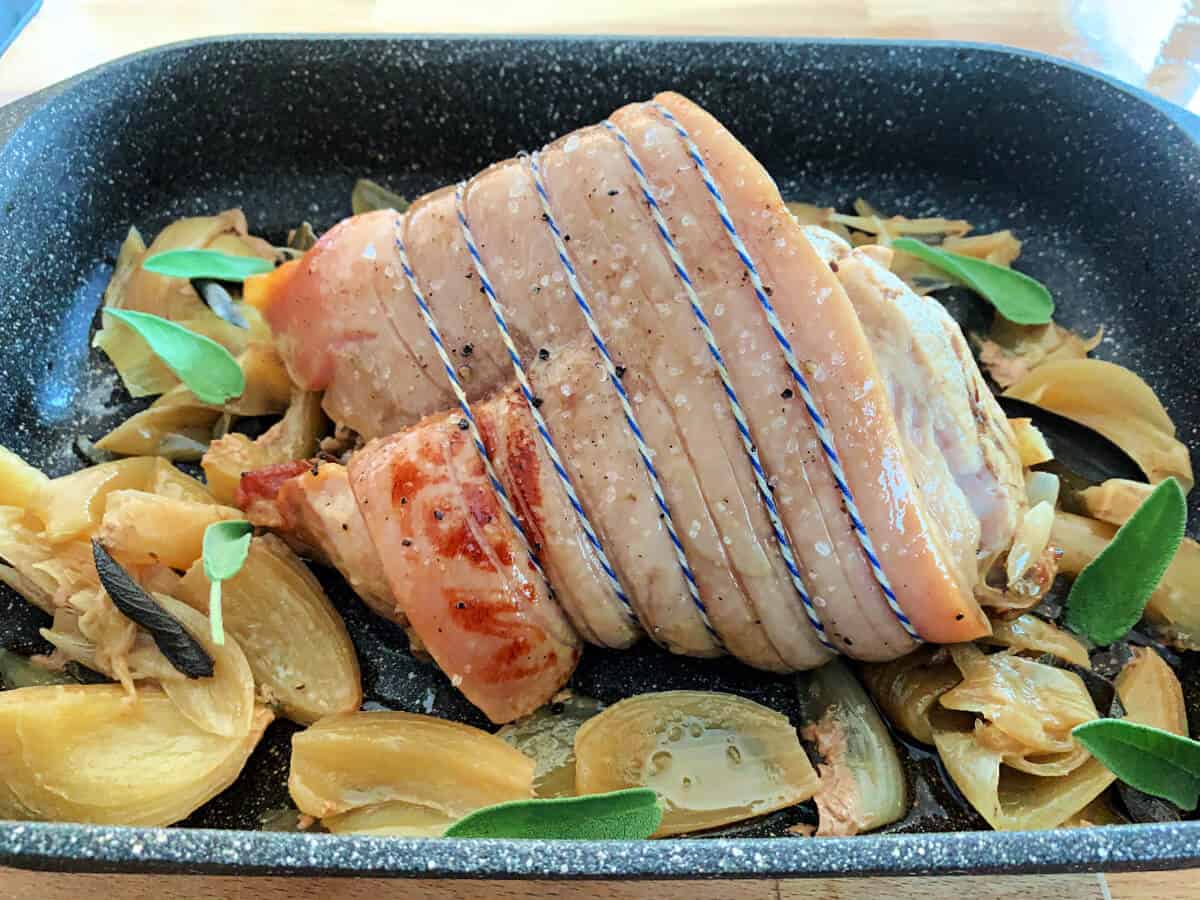 Pork joint on roasting tray with sage and onion.