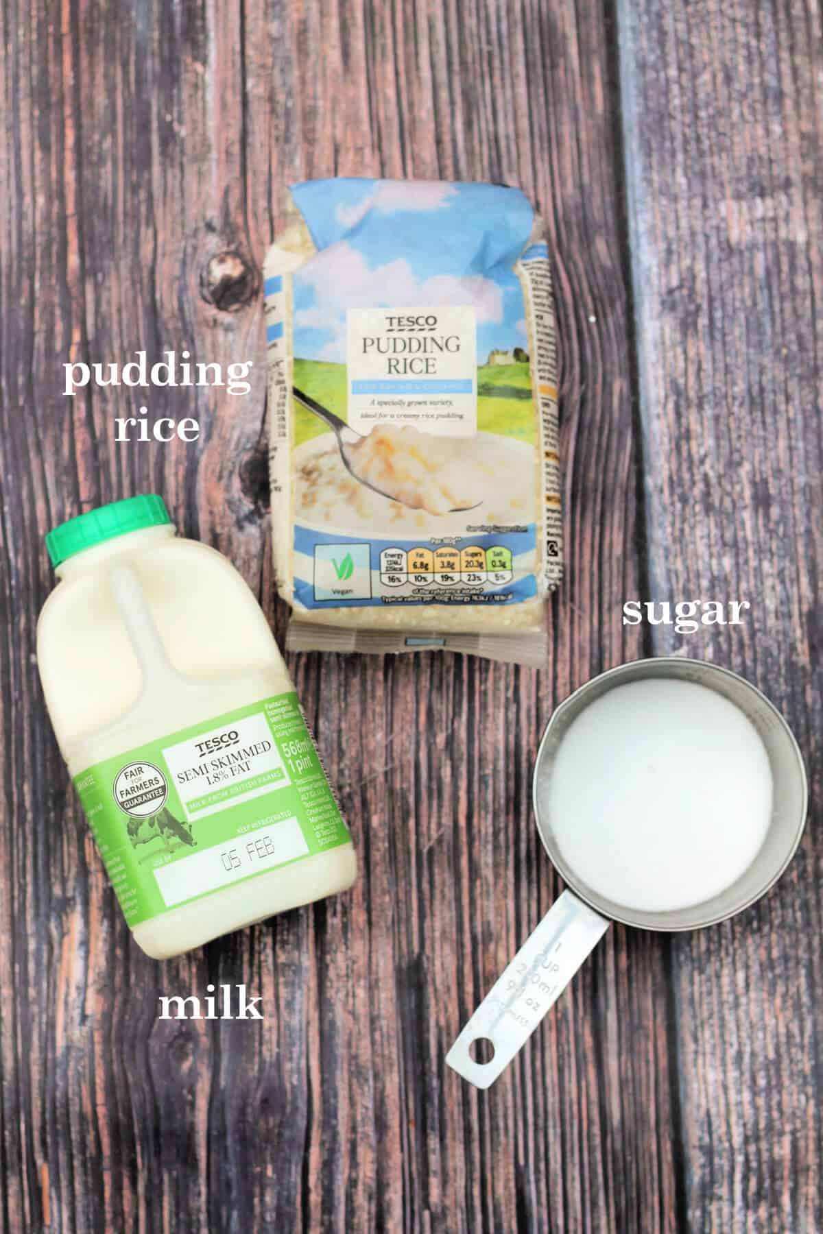 Ingredients labelled pudding rice, milk and sugar on wooden table.