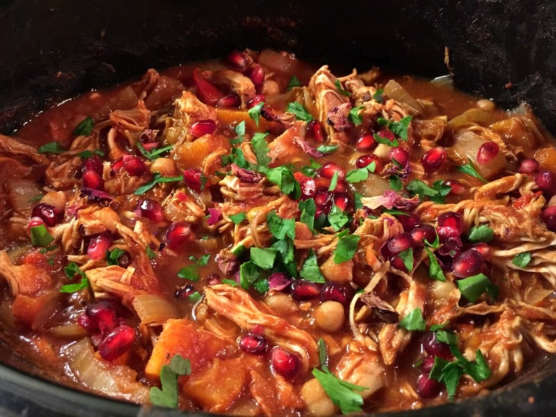 Cooked tagine in slow cooker pot, garnished with pomegranate seeds and herbs.