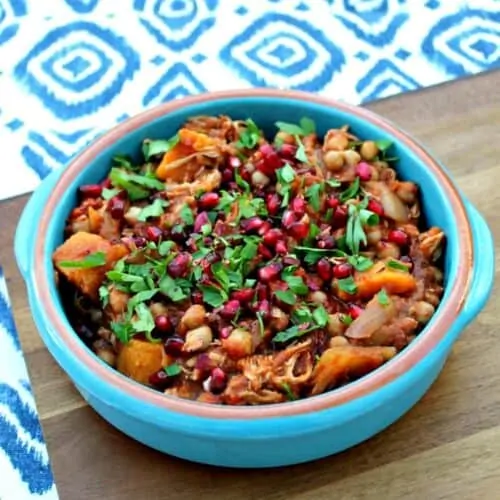 Blue bowl of chicken tagine topped with pomegranate seeds.