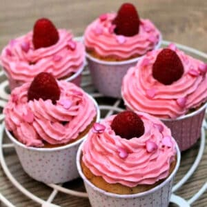 Cupcakes with pink frosting and raspberries on top on a wire cooling rack,