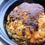 Whole cauliflower with spice rub in a slow cooker pot.