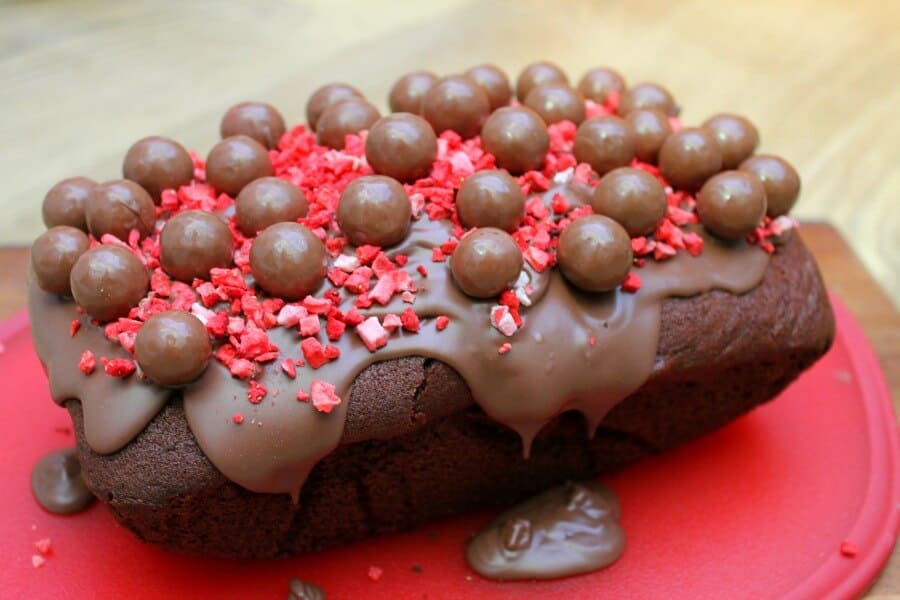 Side view of chocolate cake with chocolate icing dripping off, Maltesers and red strawberry pieces for decoration.